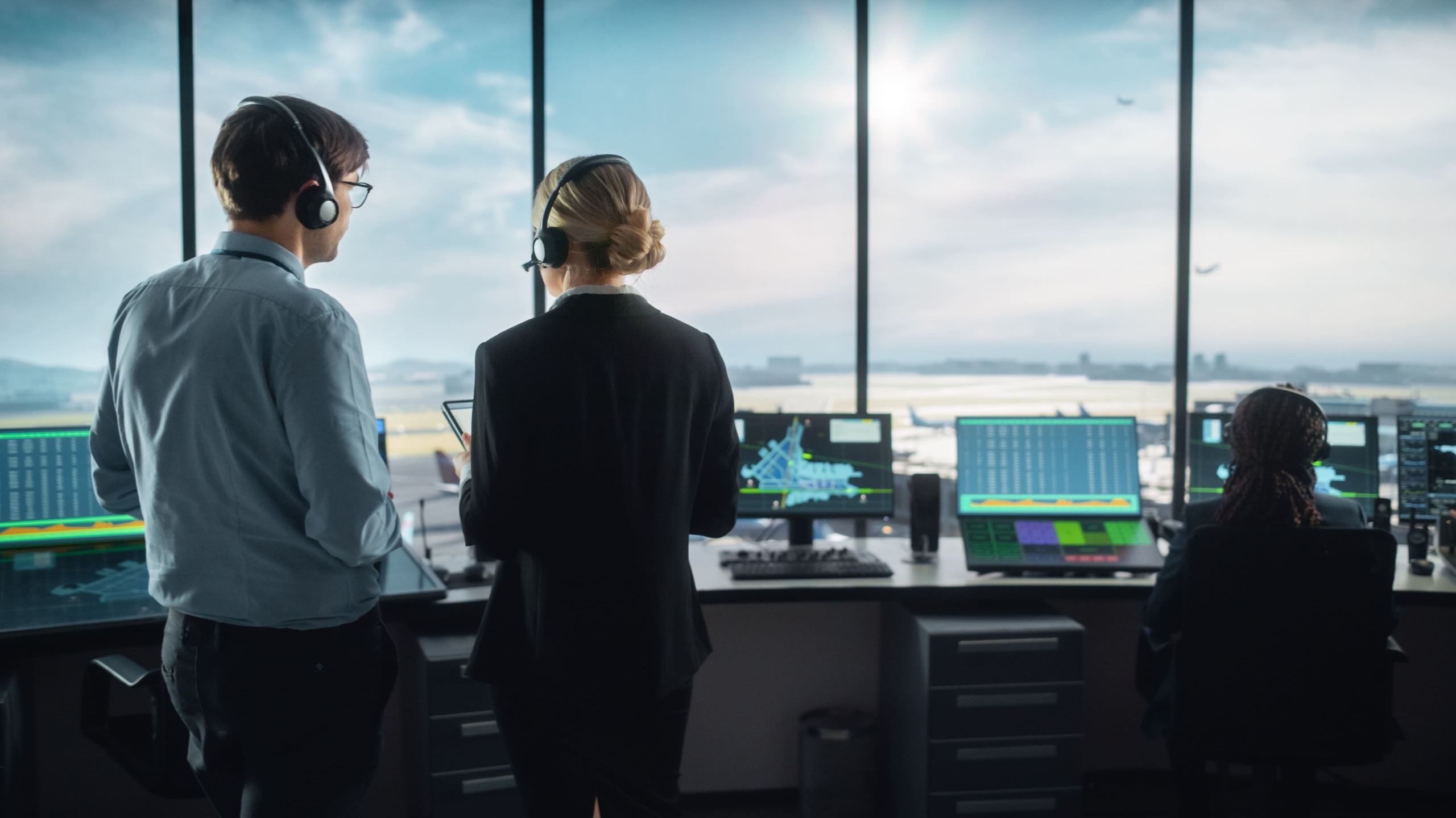 Controladores aéreos en una torre de control monitoreando pantallas de radar. Un hombre y una mujer con auriculares observan la actividad del tráfico aéreo en un entorno de alta tecnología.